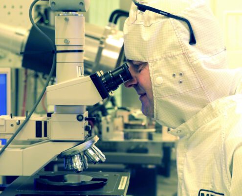 An engineer using a microscope to examine a MEMS chip wafer as part of MEMS development